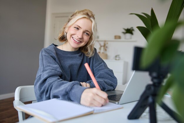 Portrait of young woman lifestyle blogger recording video of herself making notes writing in journal