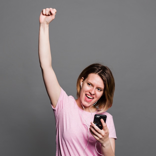 Free photo portrait of a young woman listening music on earphones through mobile phone against grey wall