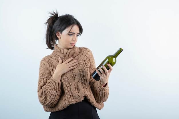 Foto gratuita ritratto di giovane donna che guarda una bottiglia di vino sul muro bianco