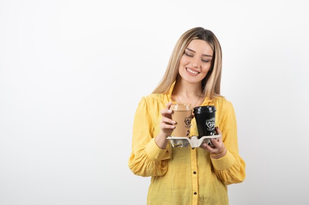 Portrait of young woman looking at cups of coffee on white background.