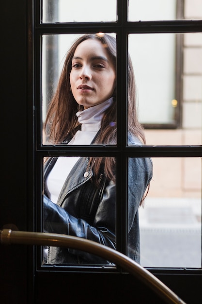 Portrait of a young woman looking out through window door