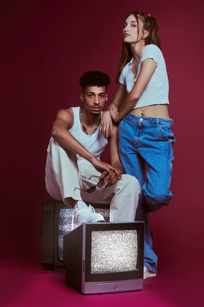 Portrait of young woman and man in 2000s fashion style posing together with tv