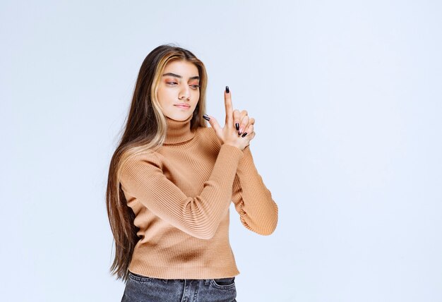 Portrait of a young woman model in brown sweater holding fingers up like a pistol.