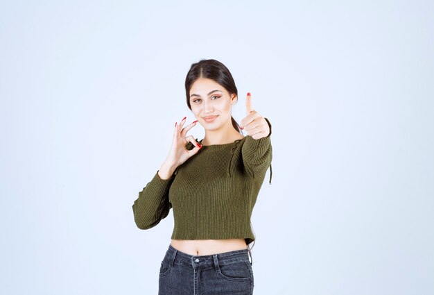 Portrait of a young woman model showing ok gesture and a thumb up.