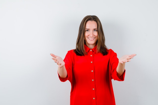 Portrait of young woman opening arms for hug in red blouse and looking merry front view