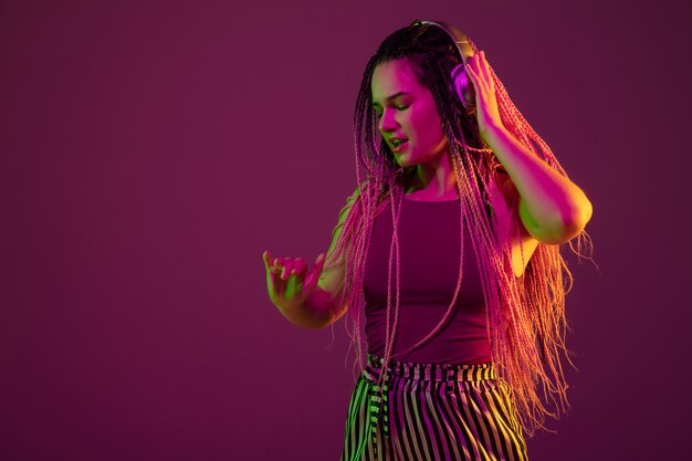 Portrait of young woman on pink wall listening to music