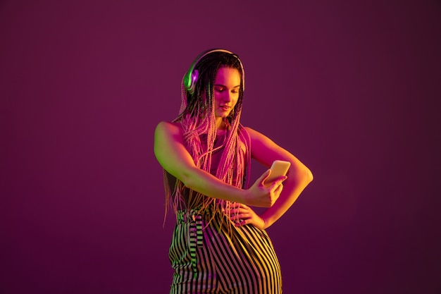 Portrait of young woman on pink wall with headphones