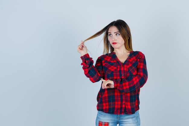 Ritratto di giovane donna che gioca con i suoi capelli in camicia a quadri e guarda pensierosa vista frontale