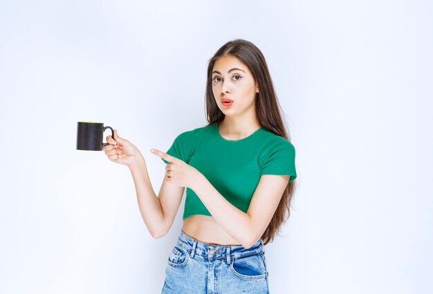 Portrait of young woman pointing at cup of tea on white background.