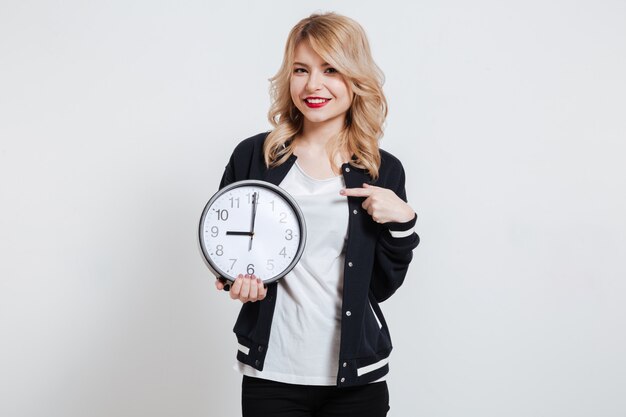 Portrait of a young woman pointing finger on wall clock