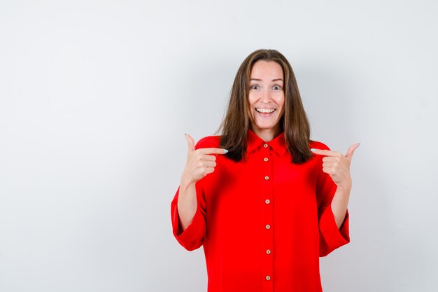 Portrait of young woman pointing at herself in red blouse and looking happy front view