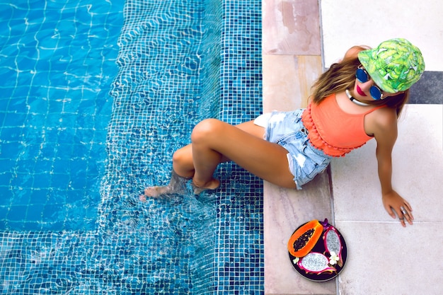 Portrait of young woman posing near pool with tropical fruits