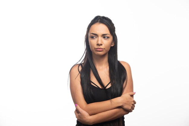 Portrait of young woman posing with crossed arms on white wall