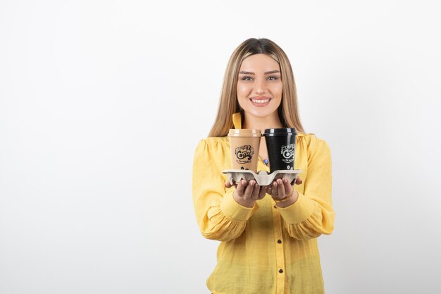 Portrait of young woman posing with cups of coffee on white background.