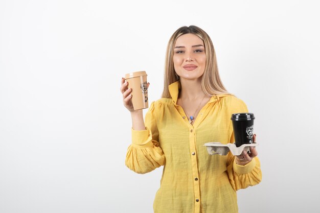 Portrait of young woman posing with cups of coffee on white.