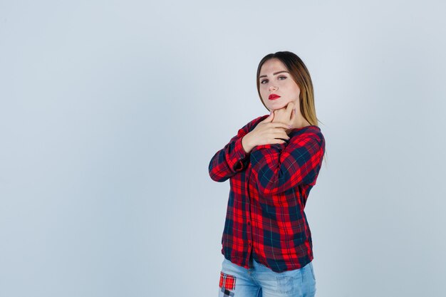 Portrait of young woman propping chin on hand in checked shirt and looking intelligent front view