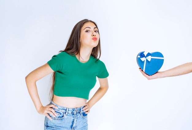 Portrait of young woman receiving blue gift box from someone on white background.