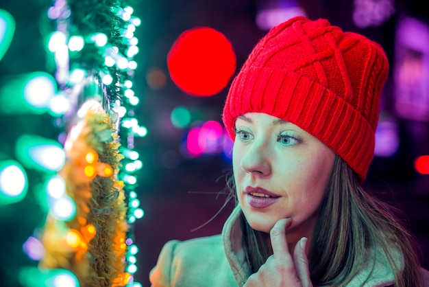Портрет молодой женщины в красной трикотажной шляпе. Счастье, зимние праздники, Рождество и люди концепции - улыбается молодая женщина в красной шляпе