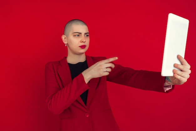 Portrait of young woman in red suit taking selfie isolated on red studio