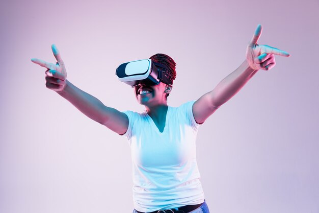 Portrait of young woman's playing in VR-glasses in neon light on gradient