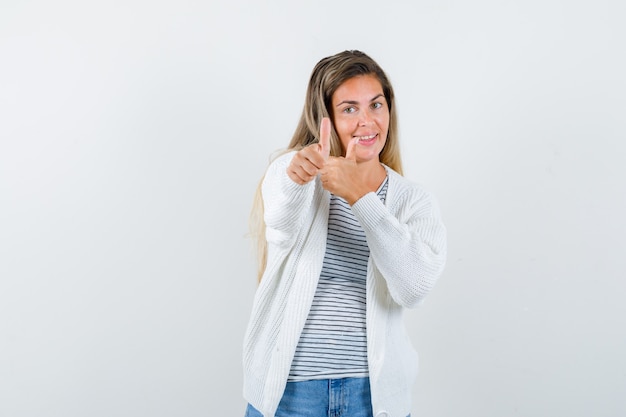 Портрет молодой женщины, показывающей двойные пальцы вверх в футболке, куртке и счастливой, вид спереди
