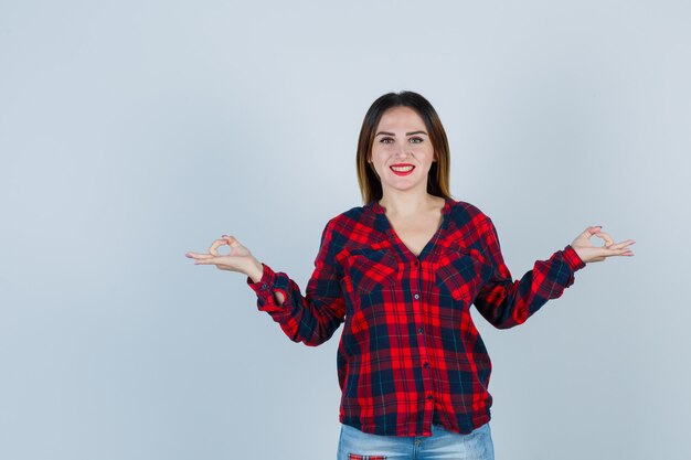 Портрет молодой женщины, показывающей жест мудры в клетчатой рубашке и веселой смотрящей спереди