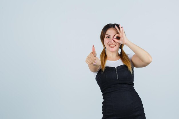 Portrait of young woman showing ok sign on eye and thumbs up