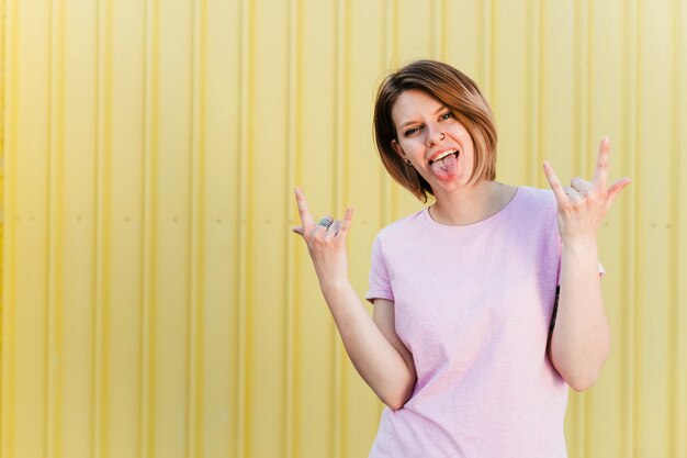 Portrait of a young woman showing rock sign and pierced tongue