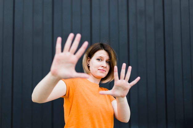 Portrait of a young woman showing stop gesture against black wall
