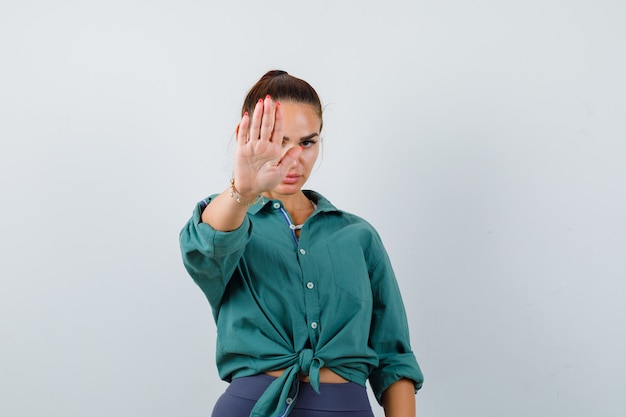 Portrait of young woman showing stop gesture in green shirt and looking annoyed front view