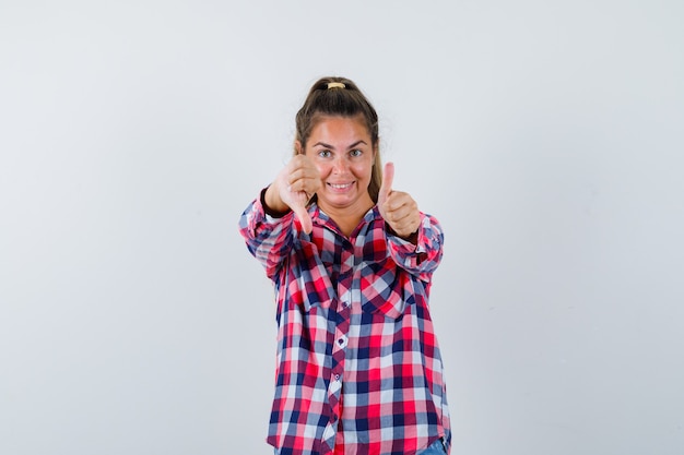 Free photo portrait of young woman showing thumbs up and down in casual shirt and looking jolly front view