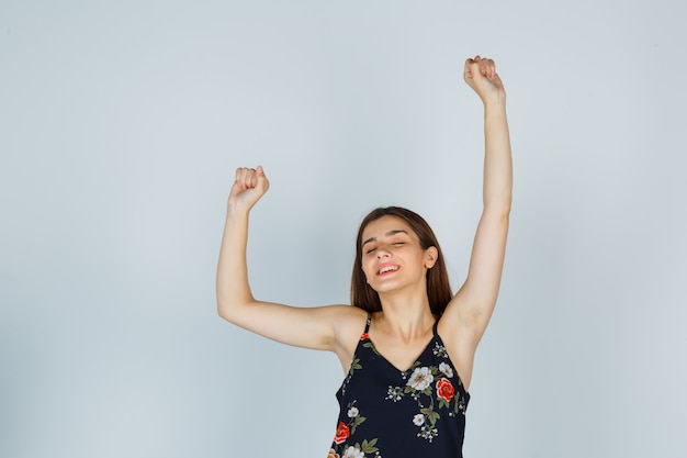 Free photo portrait of young woman showing winner gesture in blouse and looking happy front view