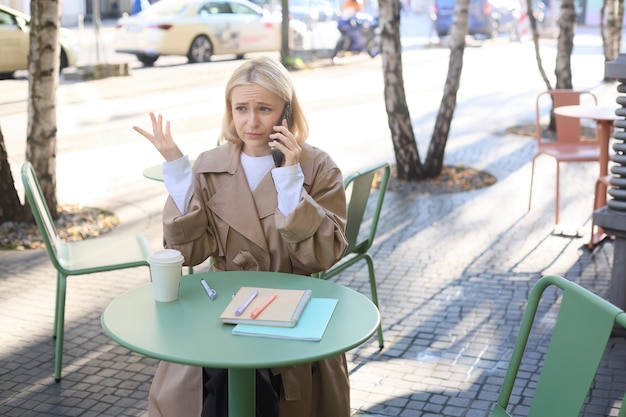 Free photo portrait of young woman sitting alone in cafe outdoors table looking upset and disappointed answer