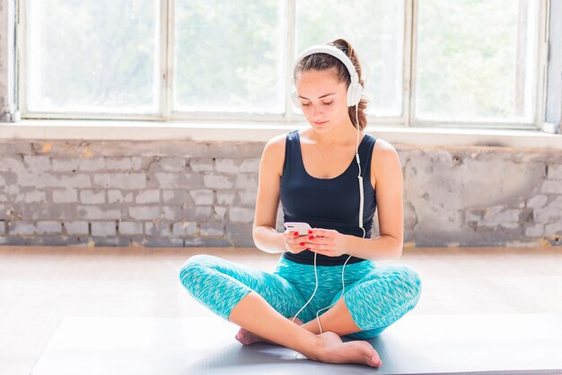 Portrait of a young woman sitting on exercise mat using cellphone