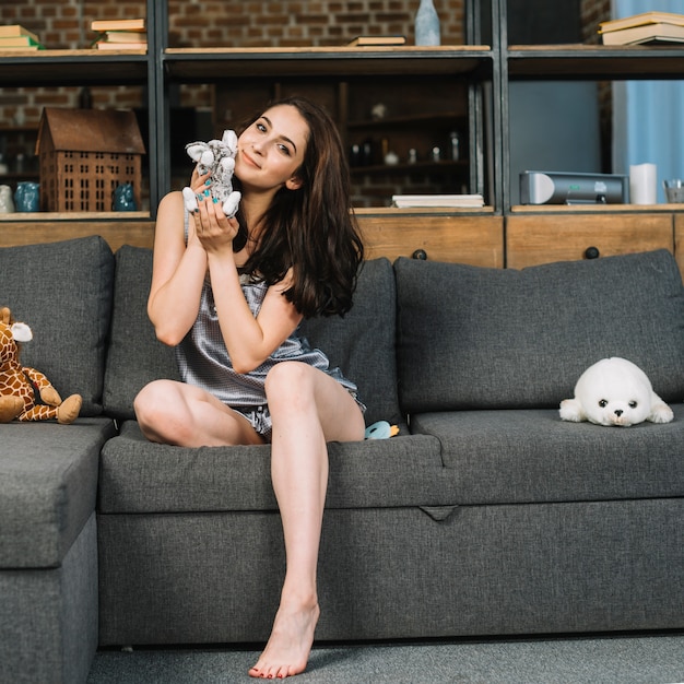 Portrait of a young woman sitting on sofa holding soft toy