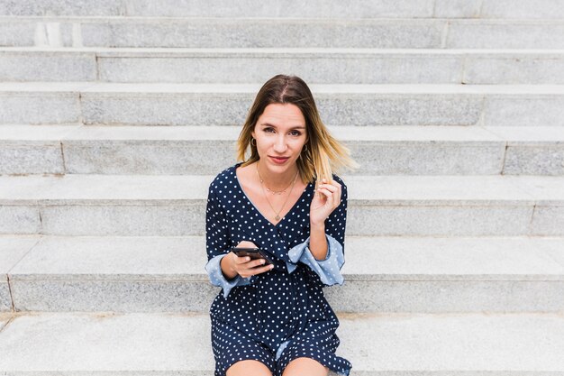Портрет молодой женщины, сидя на лестнице с мобильного телефона