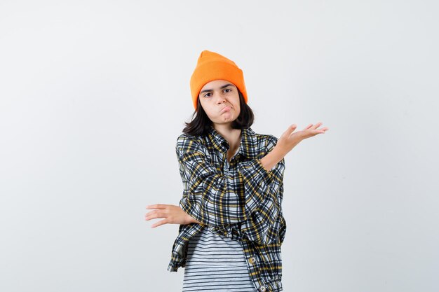 Portrait of young woman spreading palm in orange hat looking wistful