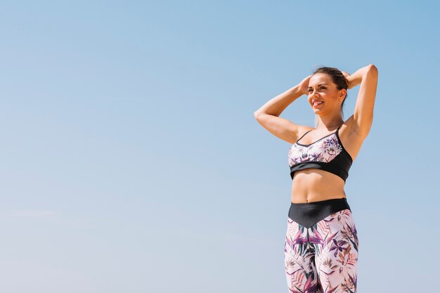 Portrait of a young woman standing against the blue sky tying her ponytail