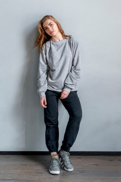 Portrait of a young woman standing against grey wall