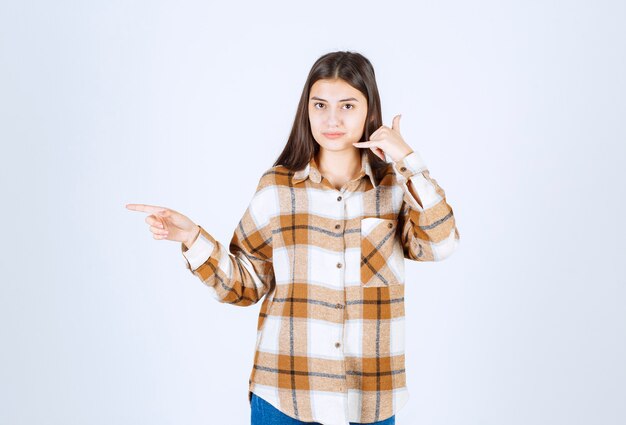 Portrait of young woman standing and pointing at somewhere on white wall. 