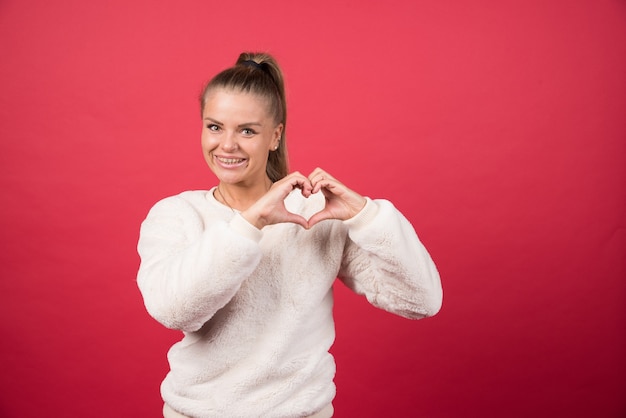 Free photo portrait of a young woman standing and showing heart