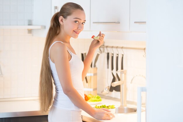 Портрет молодой женщины, дегустация зеленый салат на кухне,