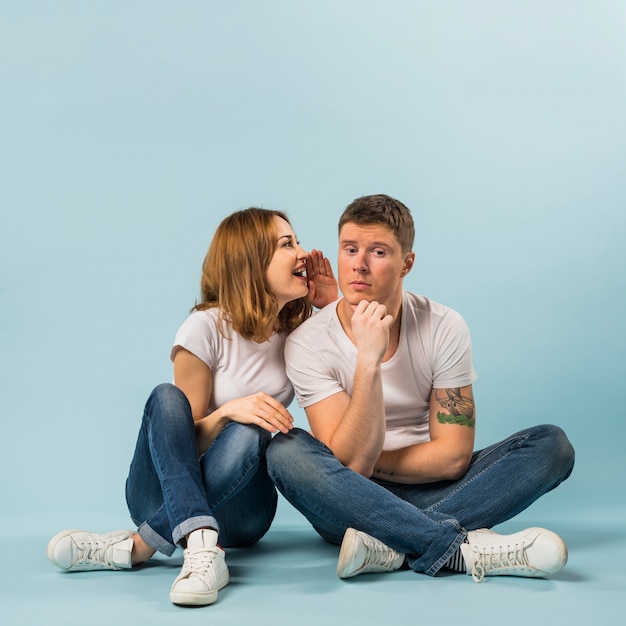 Free photo portrait of young woman telling a secret to his boyfriend against blue background