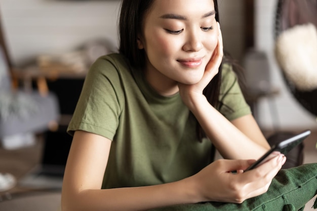 Portrait of young woman using mobile phone app from home girl sits on sofa in living room with smart...