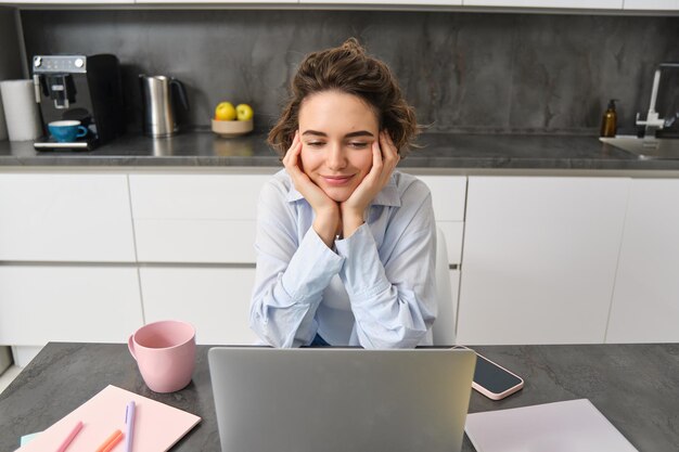 Portrait of young woman watching video on laptop looking at computer screen working from home online