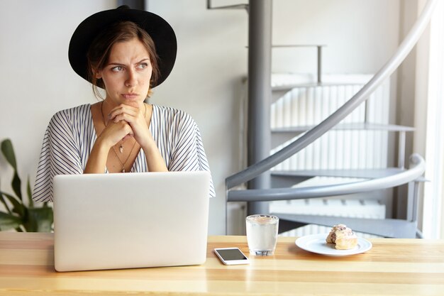 Free photo portrait of young woman wearing big hat and using laptop