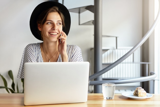 Ritratto di giovane donna che indossa un grande cappello e utilizzando laptop