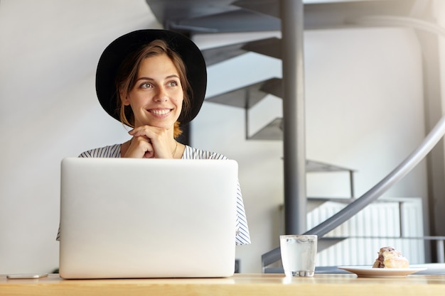 Portrait of young woman wearing big hat and using laptop