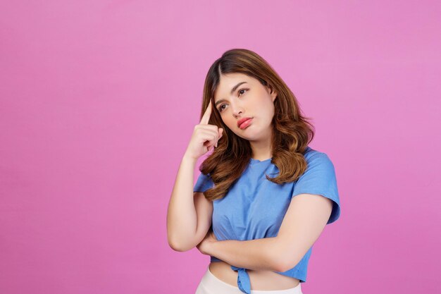 ピンクの背景に分離されたカジュアルなTシャツの思考と想像力を身に着けている若い女性の肖像画