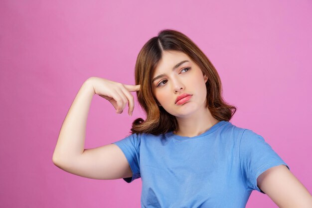 Портрет молодой женщины в повседневной футболке с мышлением и воображением, изолированным на розовом фоне